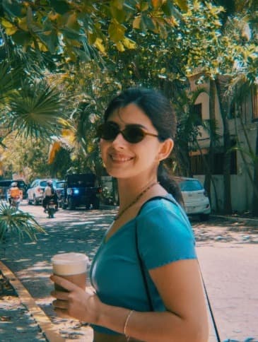 Mujer sonriendo con un café en una calle con palmeras
