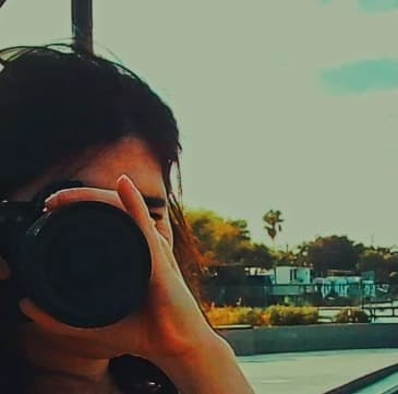Mujer fotografiando hacia la cámara junto al agua