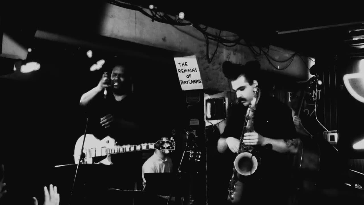 Músicos de jazz en blanco y negro bajo un letrero que dice The Remains of Tony Campise