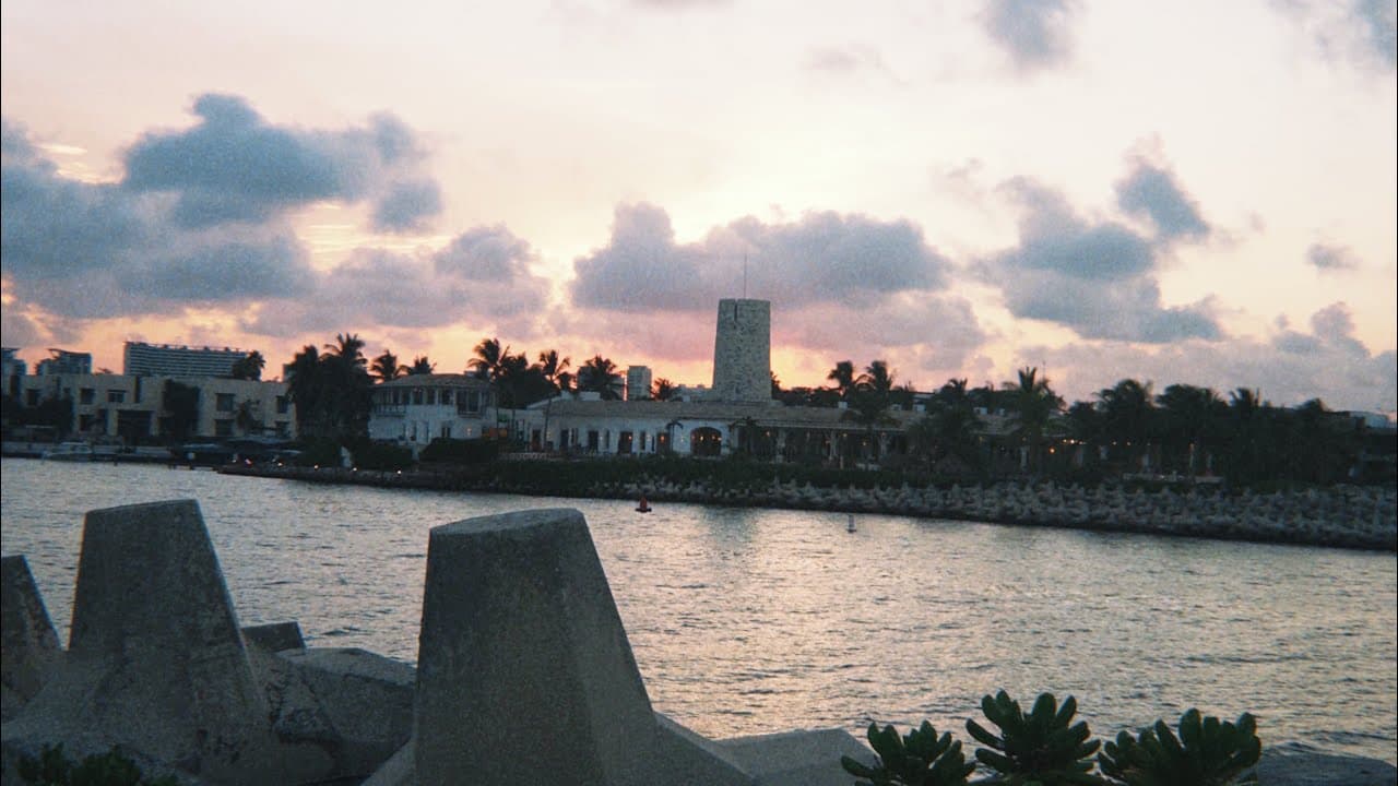 Atardecer sobre el mar con rompeolas en primer plano y casas al fondo